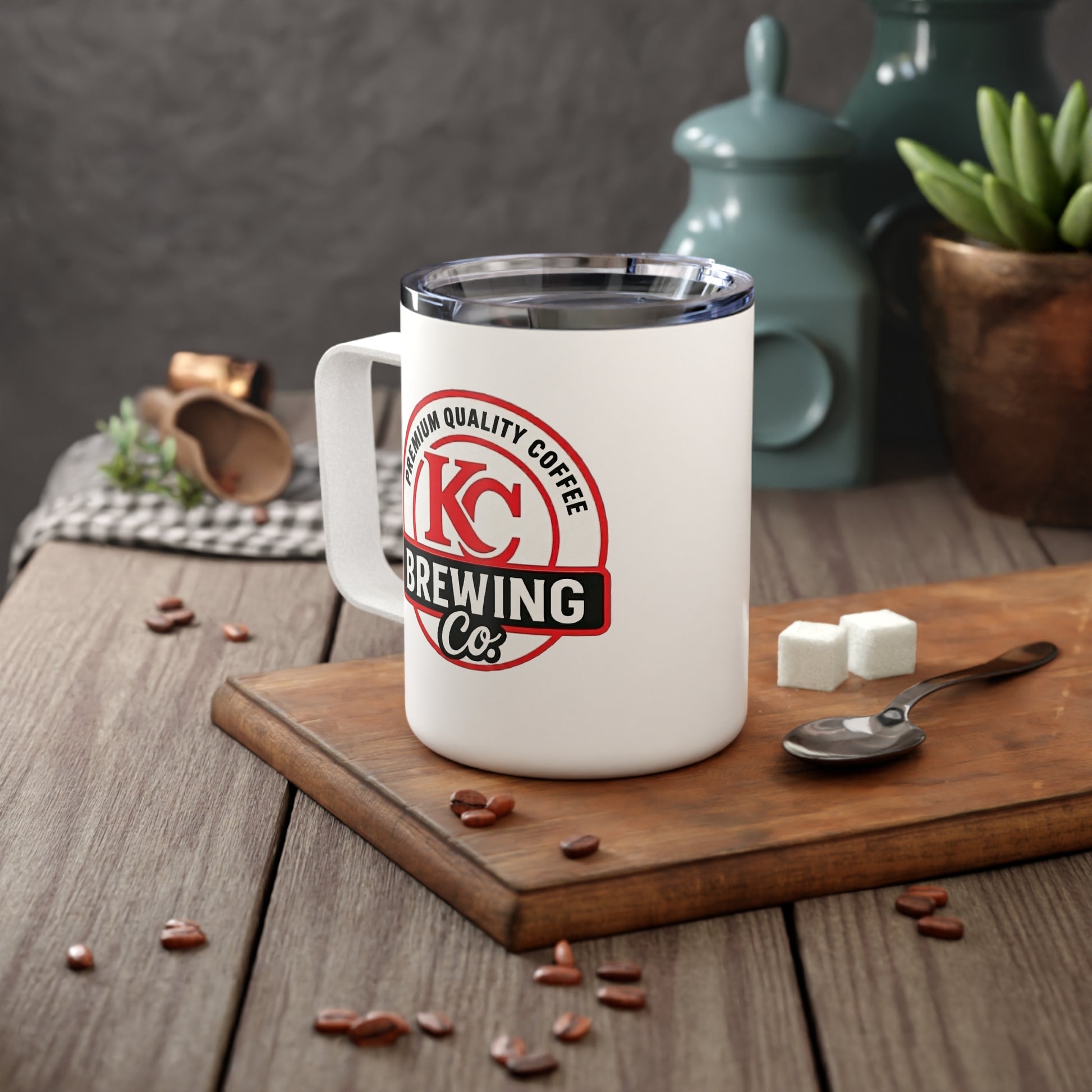 White KC Brewing Co coffee mug on wooden board with sugar cubes, spoon, coffee beans, and green jars