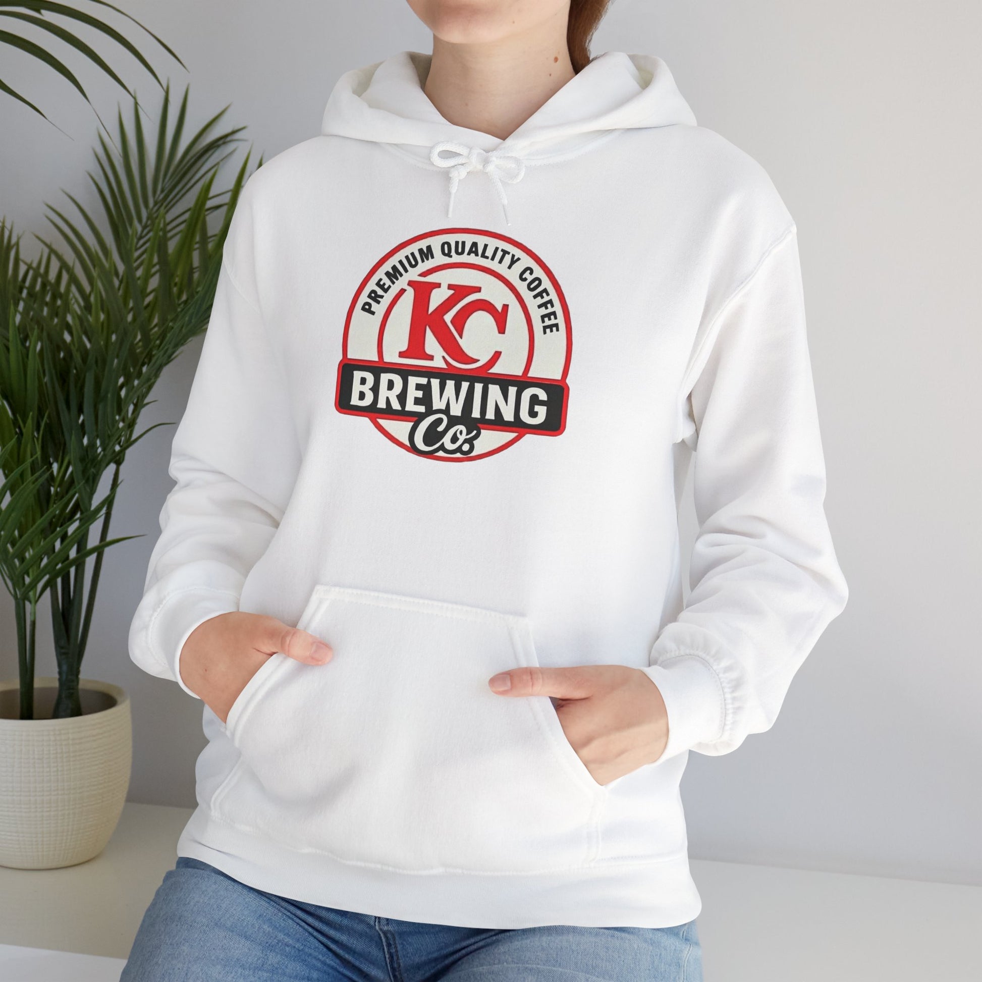 Person wearing white hoodie with KC Brewing Co premium quality coffee logo, indoor plant in background