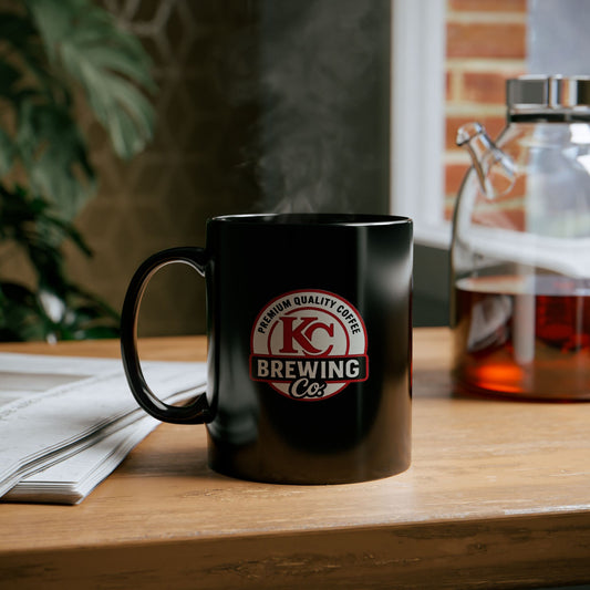 Black KC Brewing Co coffee mug with steam, wooden table, newspaper, and glass coffee pot